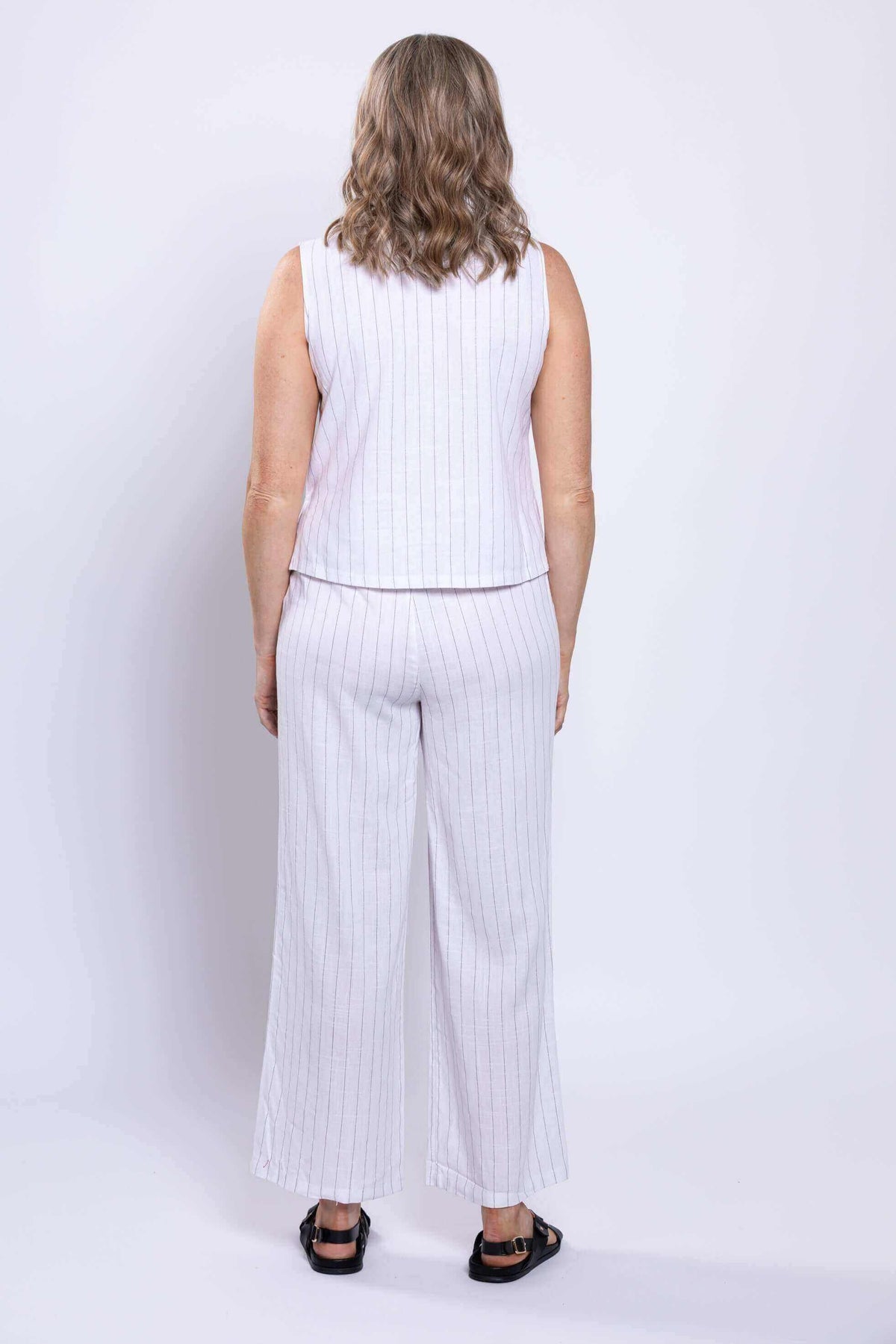 Back view of woman wearing white striped sleeveless linen blend tank and matching pants