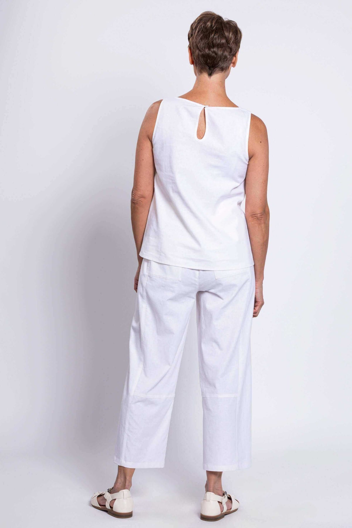 Back view of woman wearing white tank top with button closure and white pants