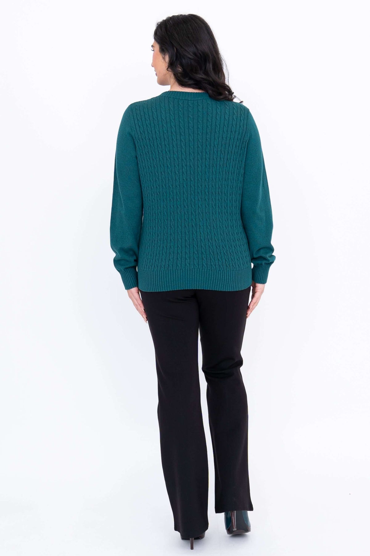 Back view of a woman in a teal cable knit sweater with ribbed hem, wearing black pants