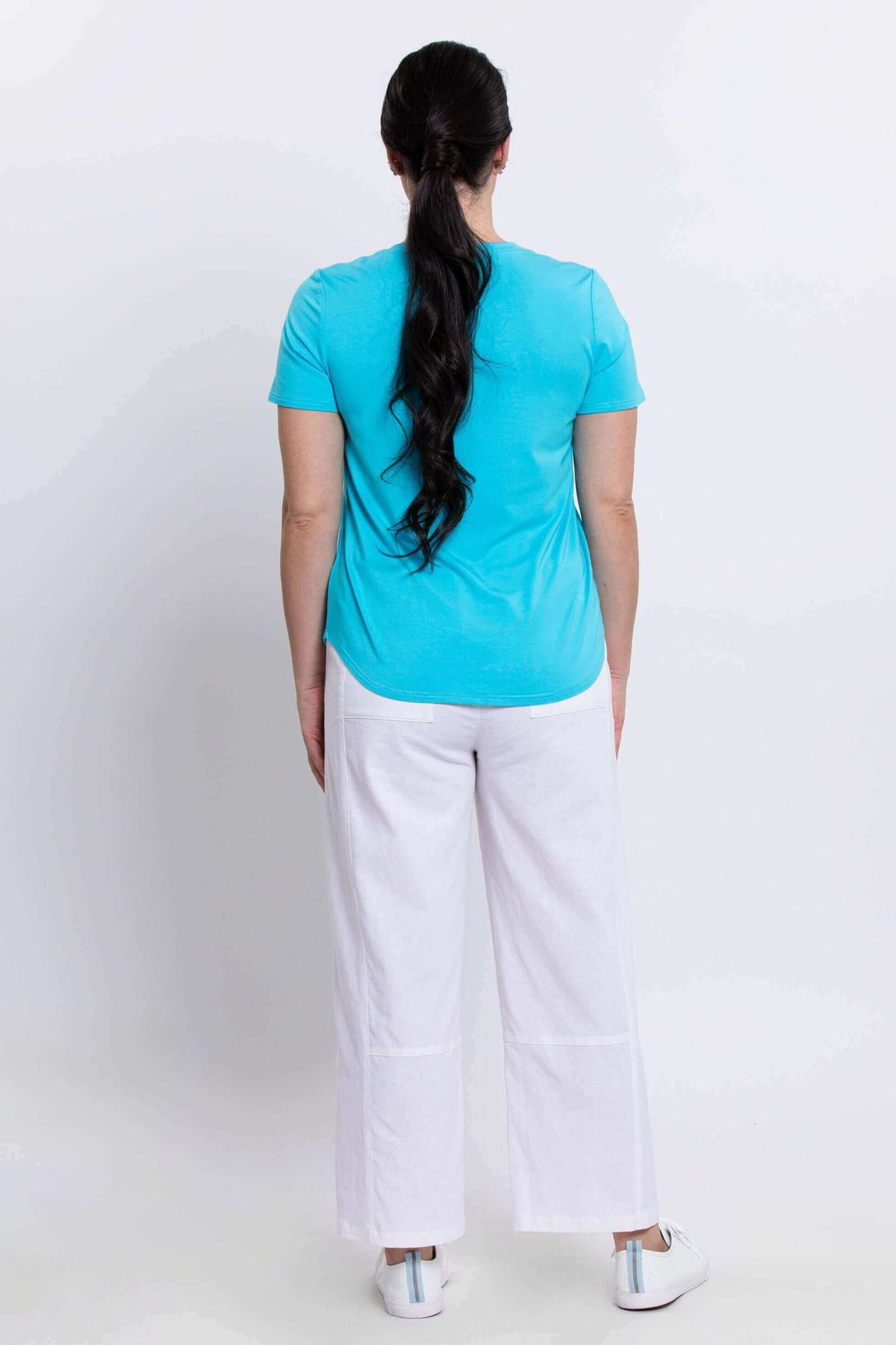 Back view of woman in turquoise tee and white pants, hair in ponytail