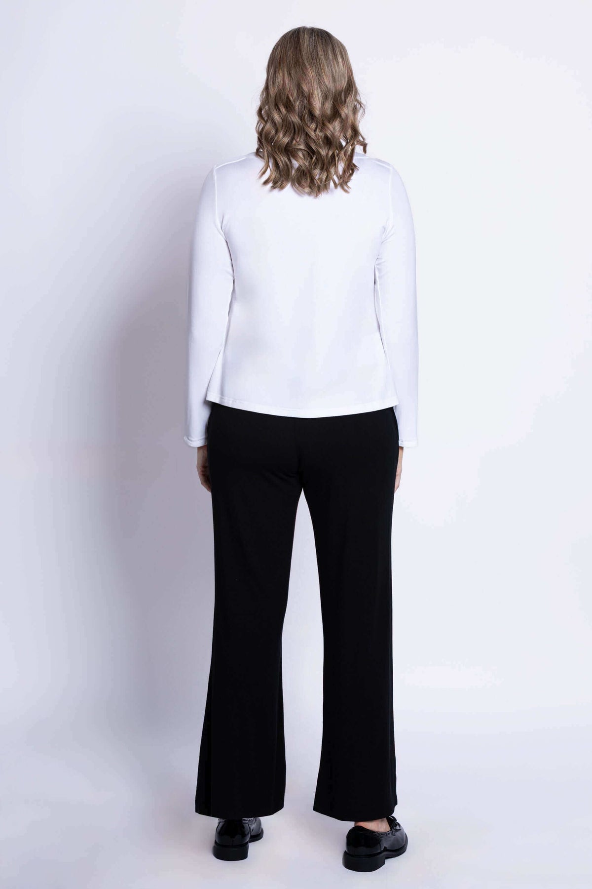 Back view of woman in white long sleeve top and black pants