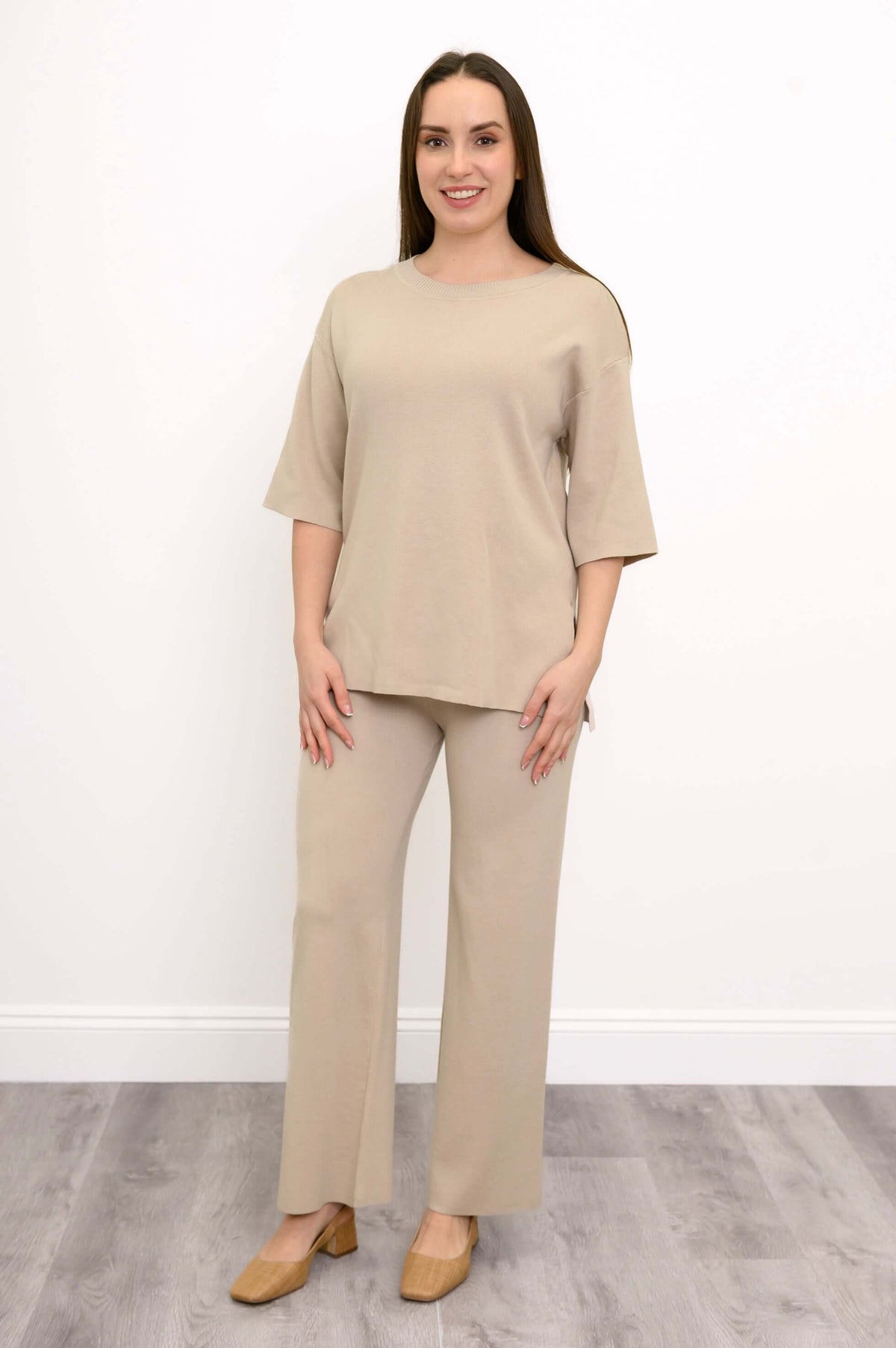 Full length view of a woman wearing tan wide leg knit pants with a matching beige sweater and tan shoes.