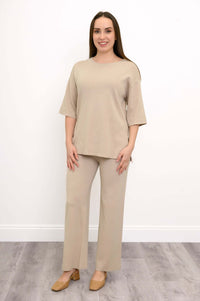 Full length view of a woman wearing tan wide leg knit pants with a matching beige sweater and tan shoes.
