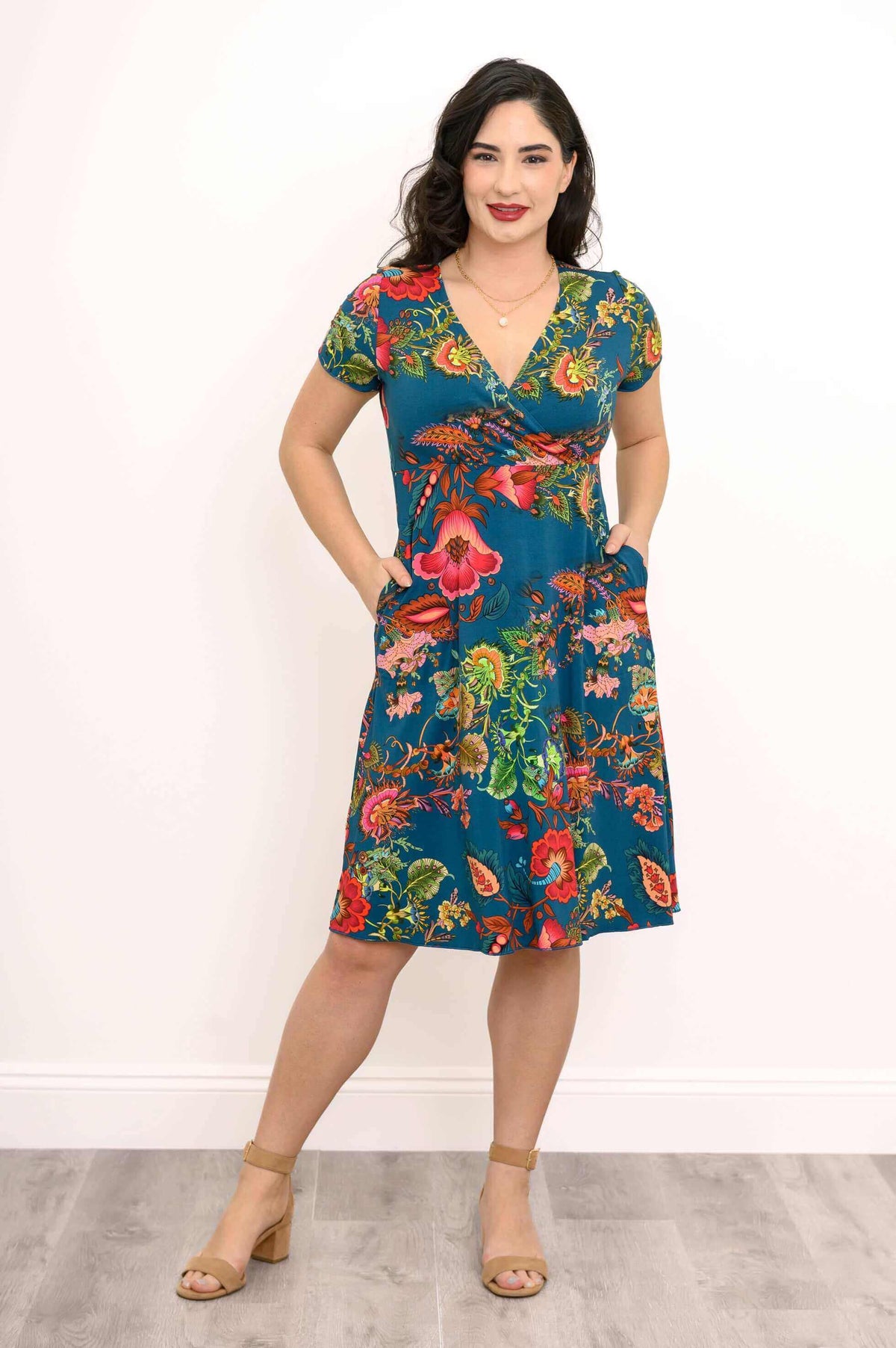 Woman standing with hands in pockets, in a teal floral bamboo wrap dress