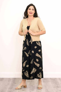 Woman layering a beige cardigan over a black patterned jumpsuit