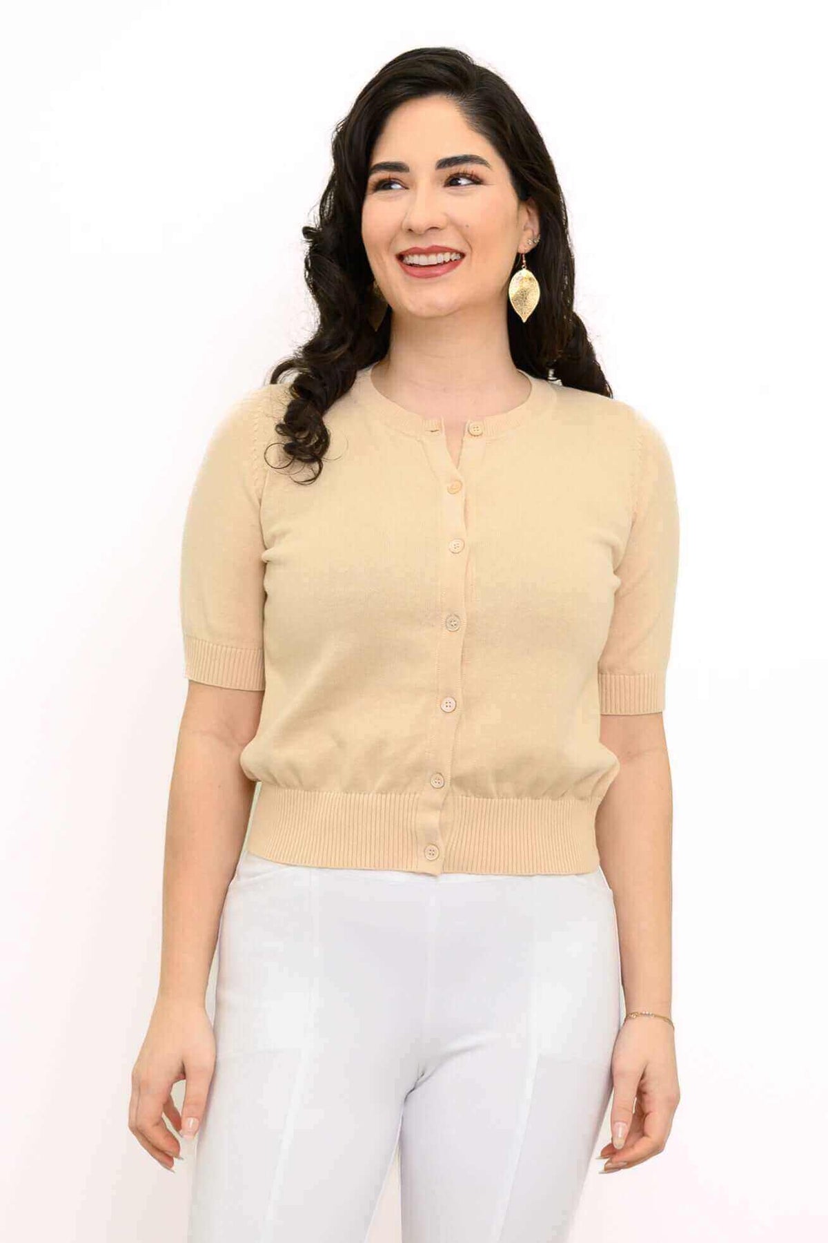 Woman wearing a beige short-sleeve cardigan with white pants, smiling