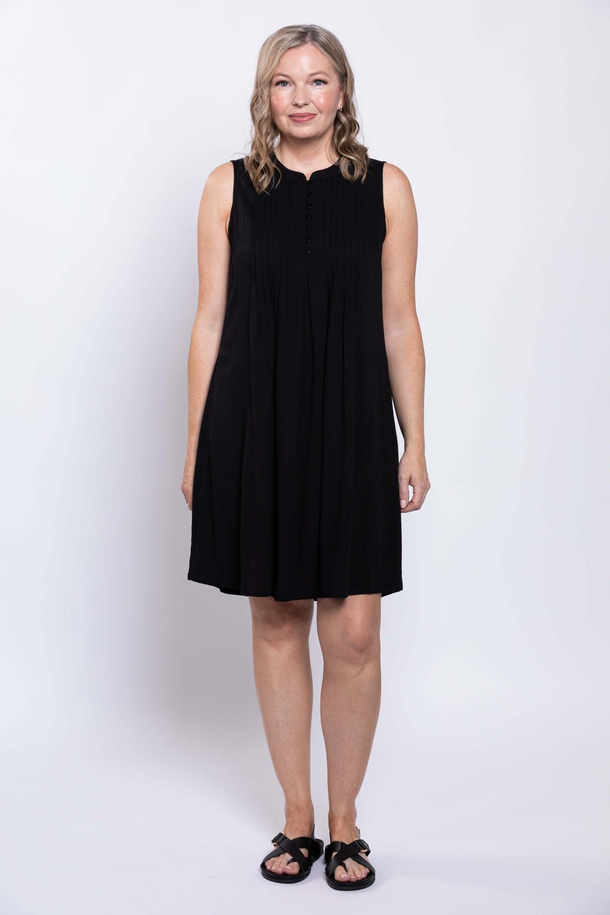 Front view of woman in a sleeveless black A-line dress with pintuck details