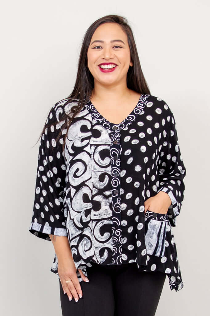 Woman smiling in a black and white V-neck top with swirl and polka dot patterns