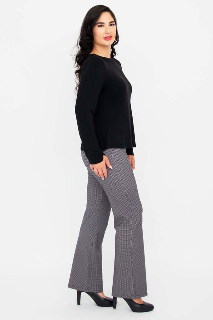 Woman standing sideways in black boat neck top and gray check pants