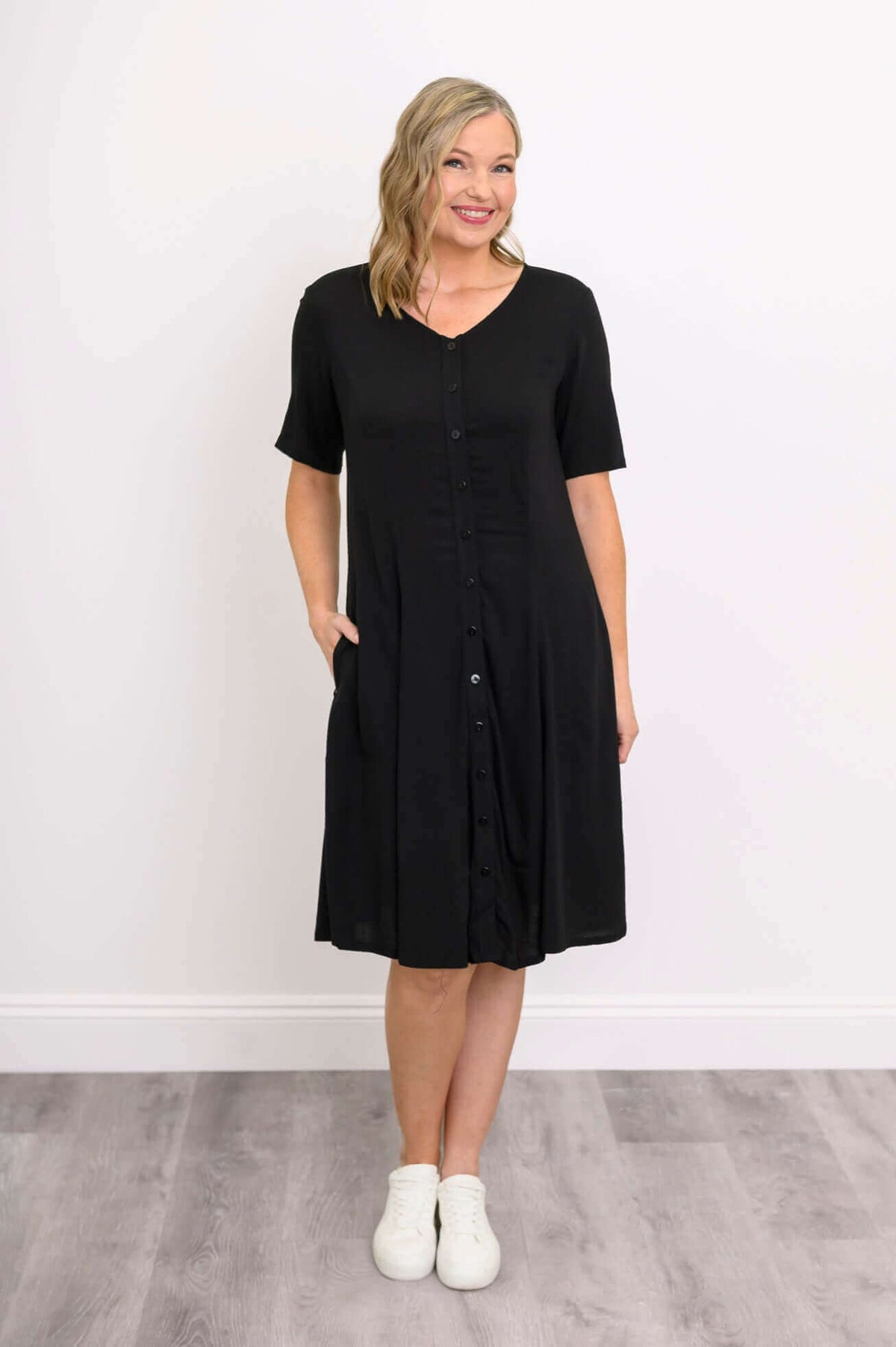 Woman wearing a black button-up dress with short sleeves and pockets, front view