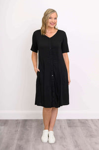 Woman wearing a black button-up dress with short sleeves and pockets, front view