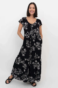 Woman posing in a black floral tiered maxi dress with side pockets and short flutter sleeves