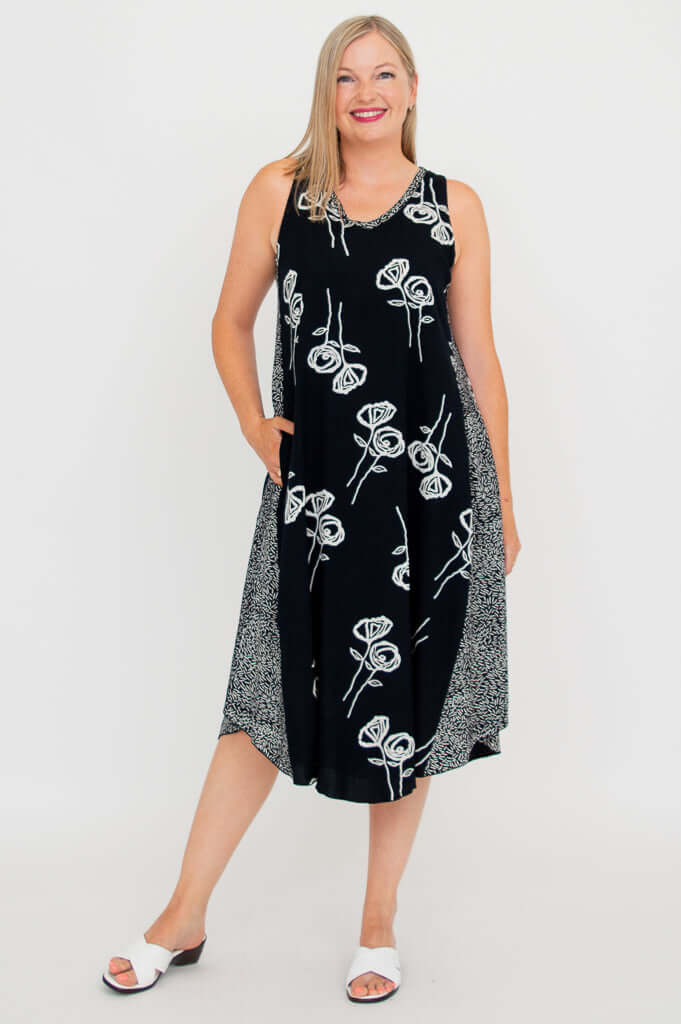 Woman wearing black tank dress with white botanical pattern, left hand in pocket