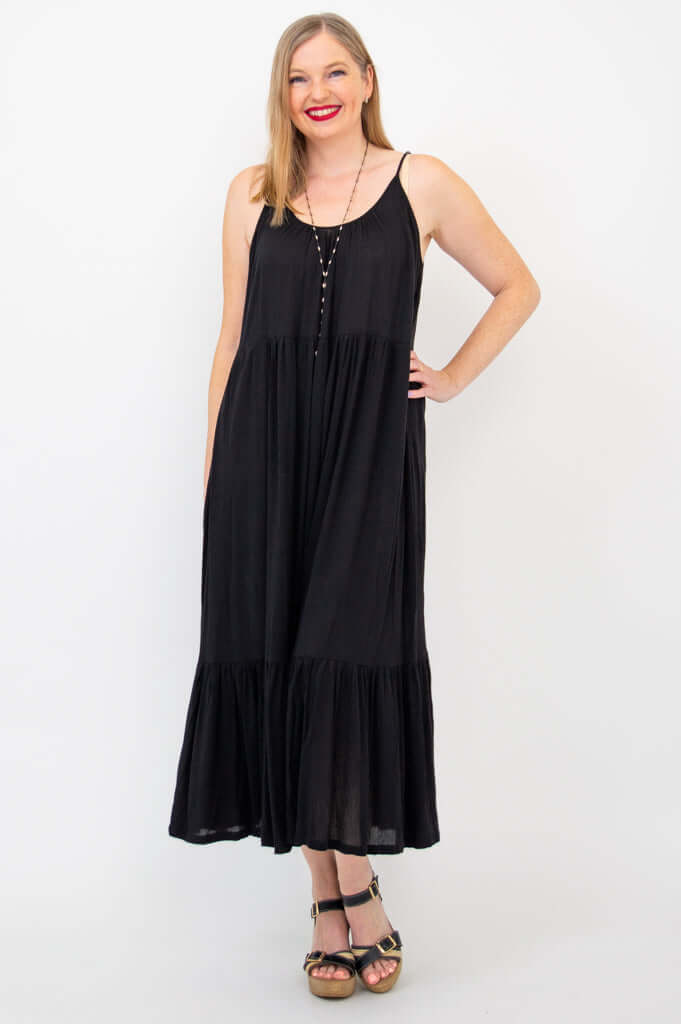 Woman wearing a black tiered maxi dress with adjustable spaghetti straps and sandals