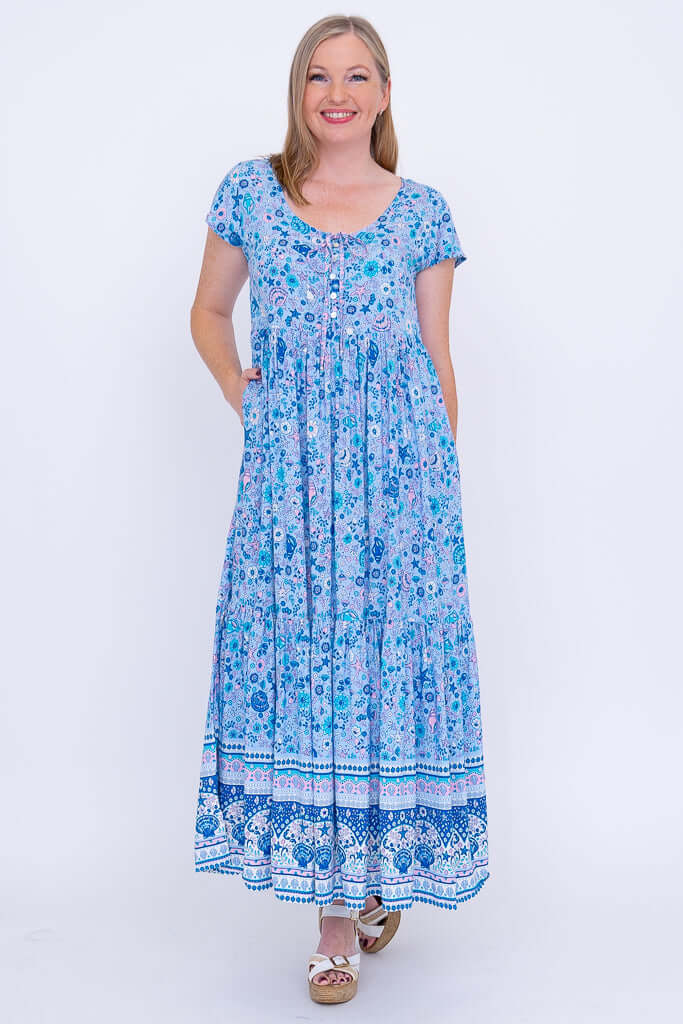 Woman standing in blue printed maxi dress with hands in pockets, front view