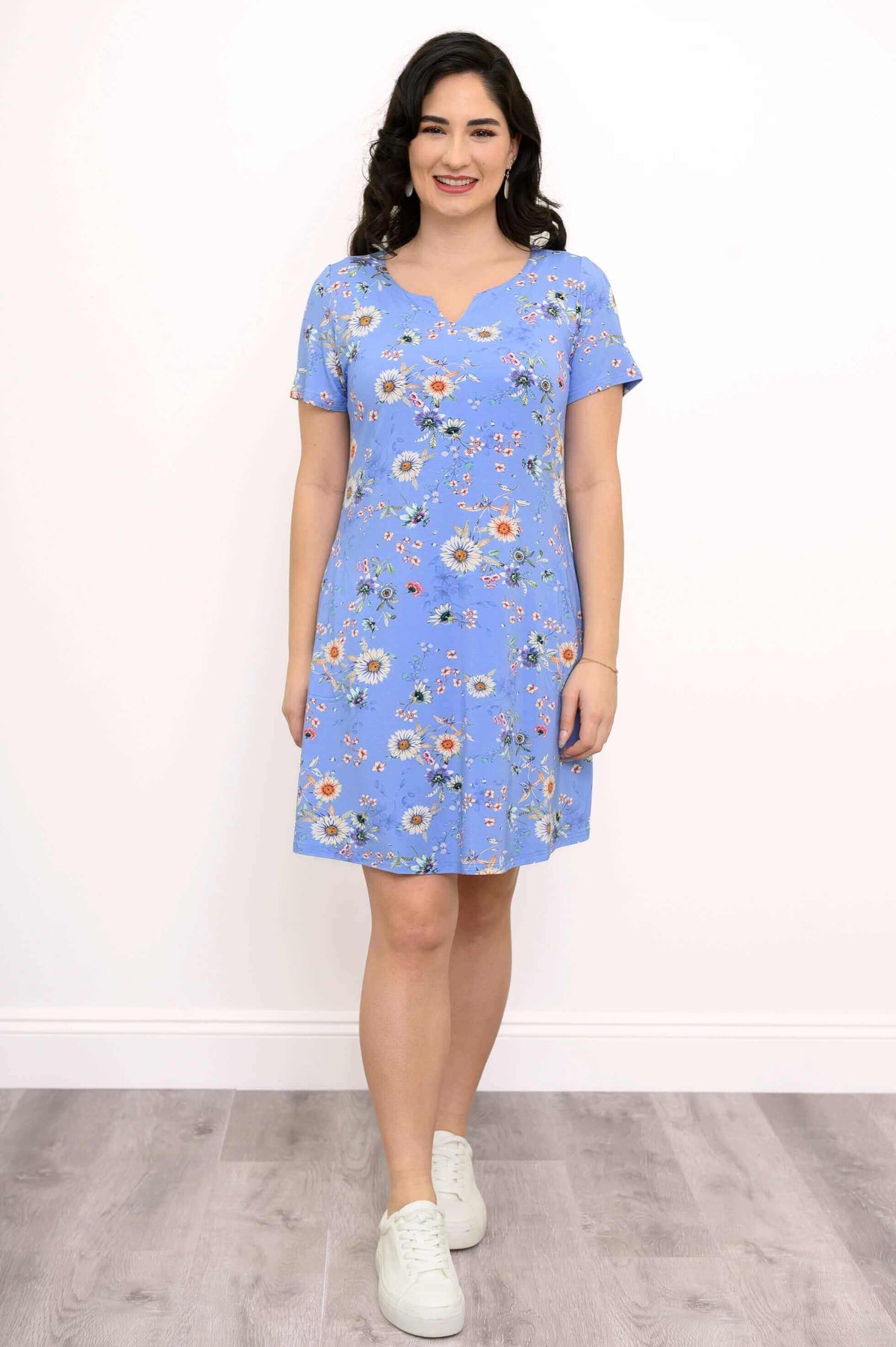 Woman wearing a blue floral A-line shift dress with white sneakers, front view