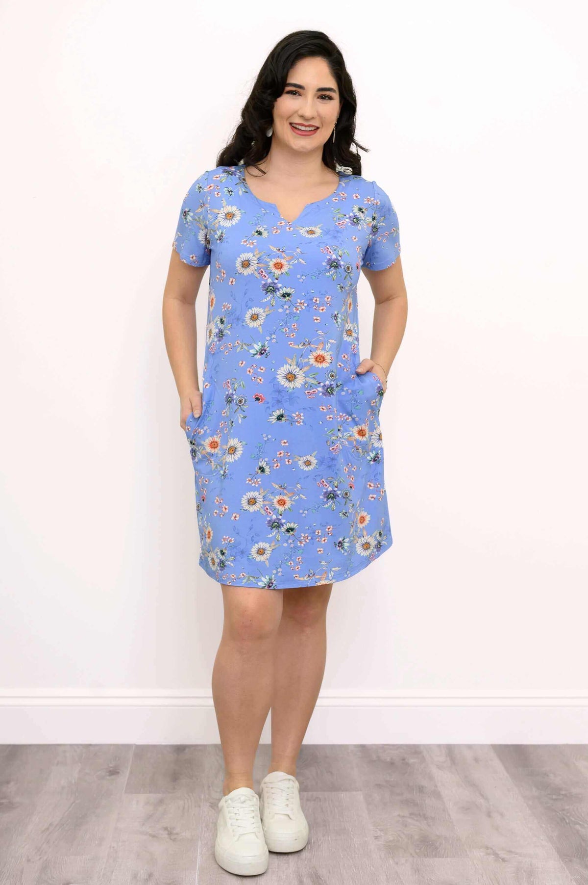 Woman smiling in blue floral A-line shift dress with hands in pockets, front view