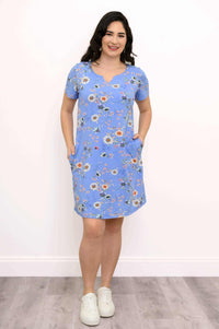 Woman smiling in blue floral A-line shift dress with hands in pockets, front view