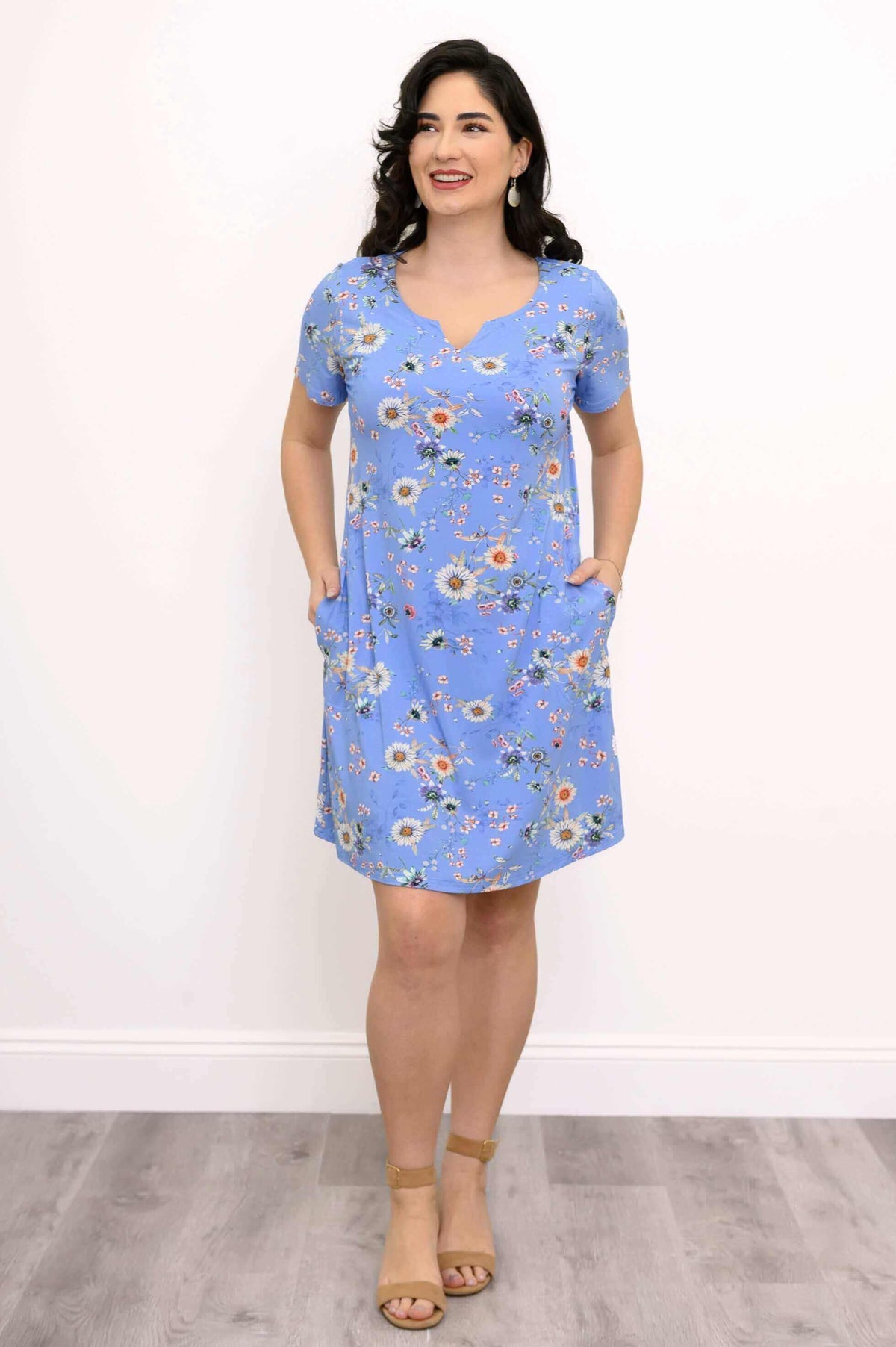 Woman in blue floral shift dress with hands in pockets, smiling, front view