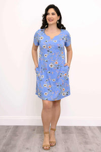 Woman in blue floral shift dress with hands in pockets, smiling, front view