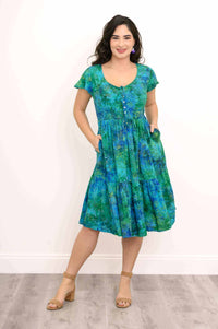 Woman in blue and green floral dress with hands in pockets, smiling