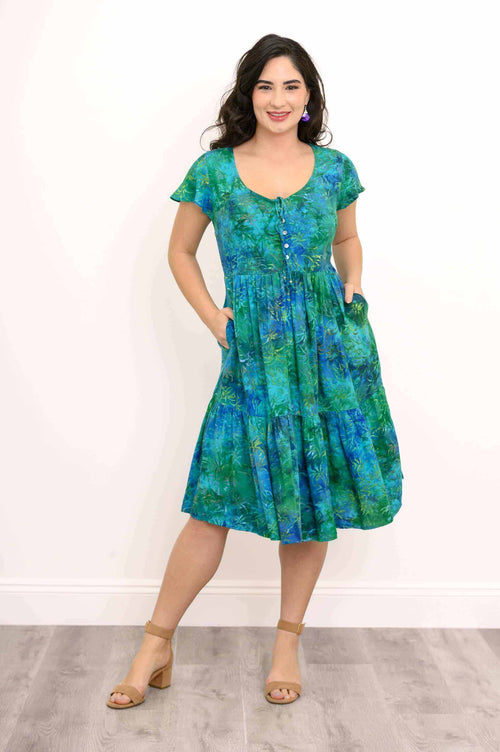 Woman in blue and green floral dress with hands in pockets, smiling