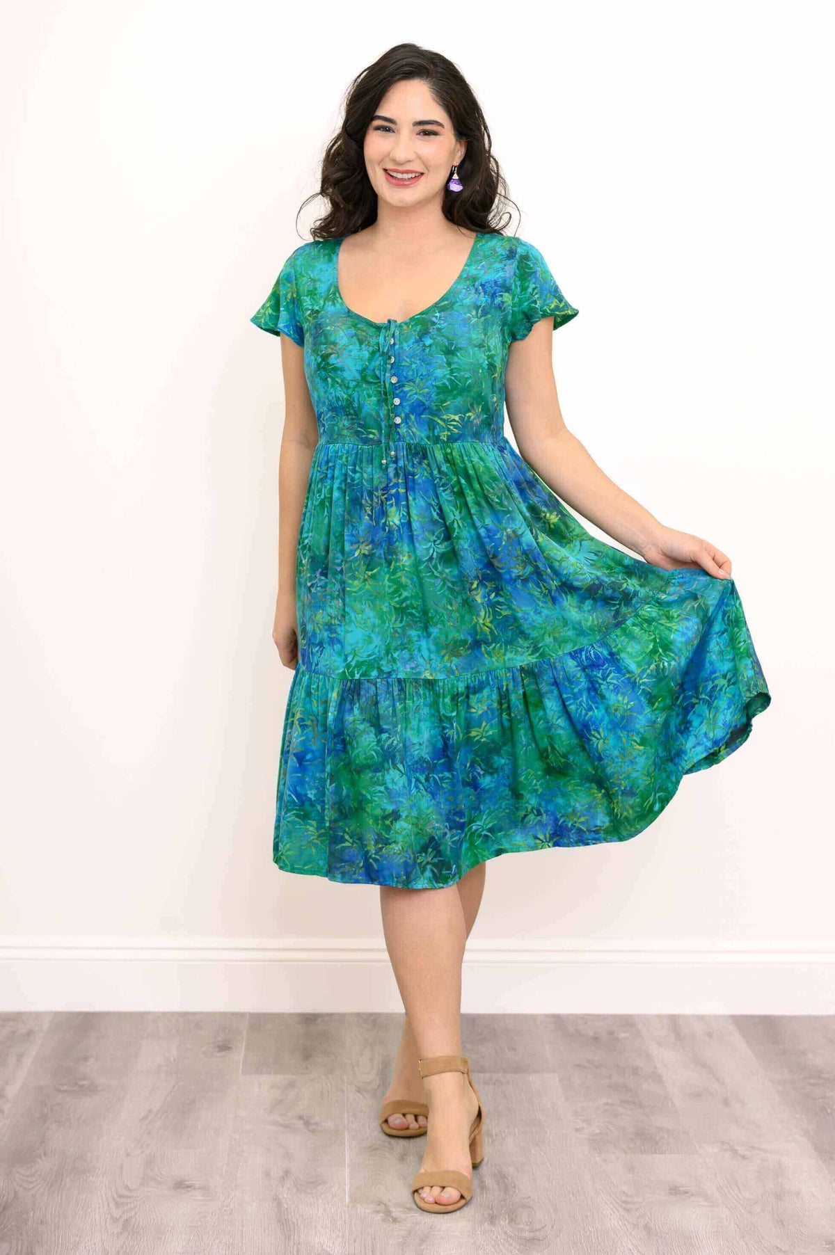 Woman holding out skirt of blue and green tiered dress, smiling