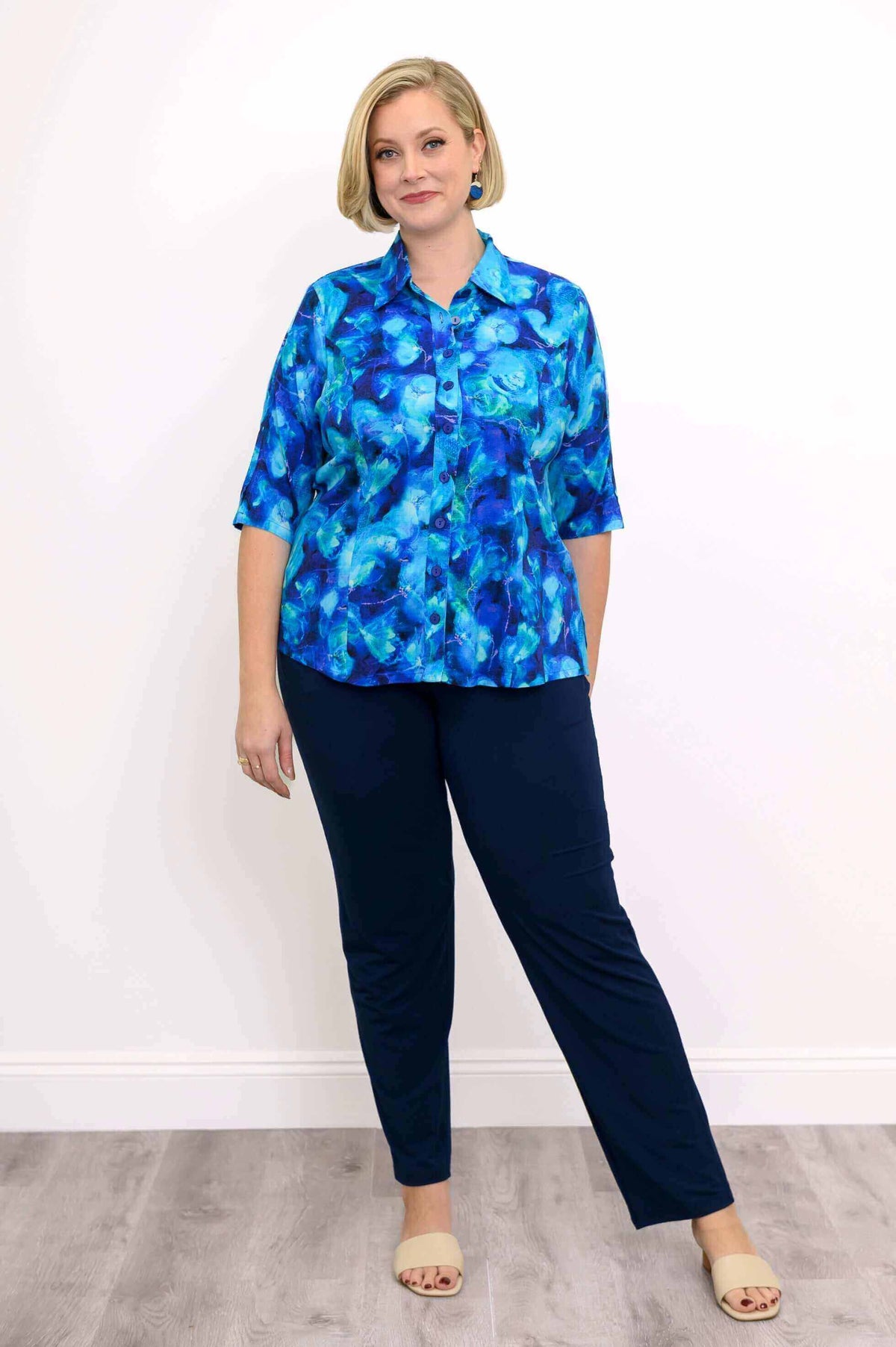Model in a blue blouse and navy pants standing on wood flooring