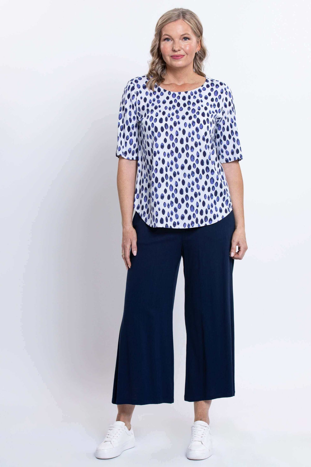 Woman standing in a blue dapple dot print blouse with wide-leg navy pants