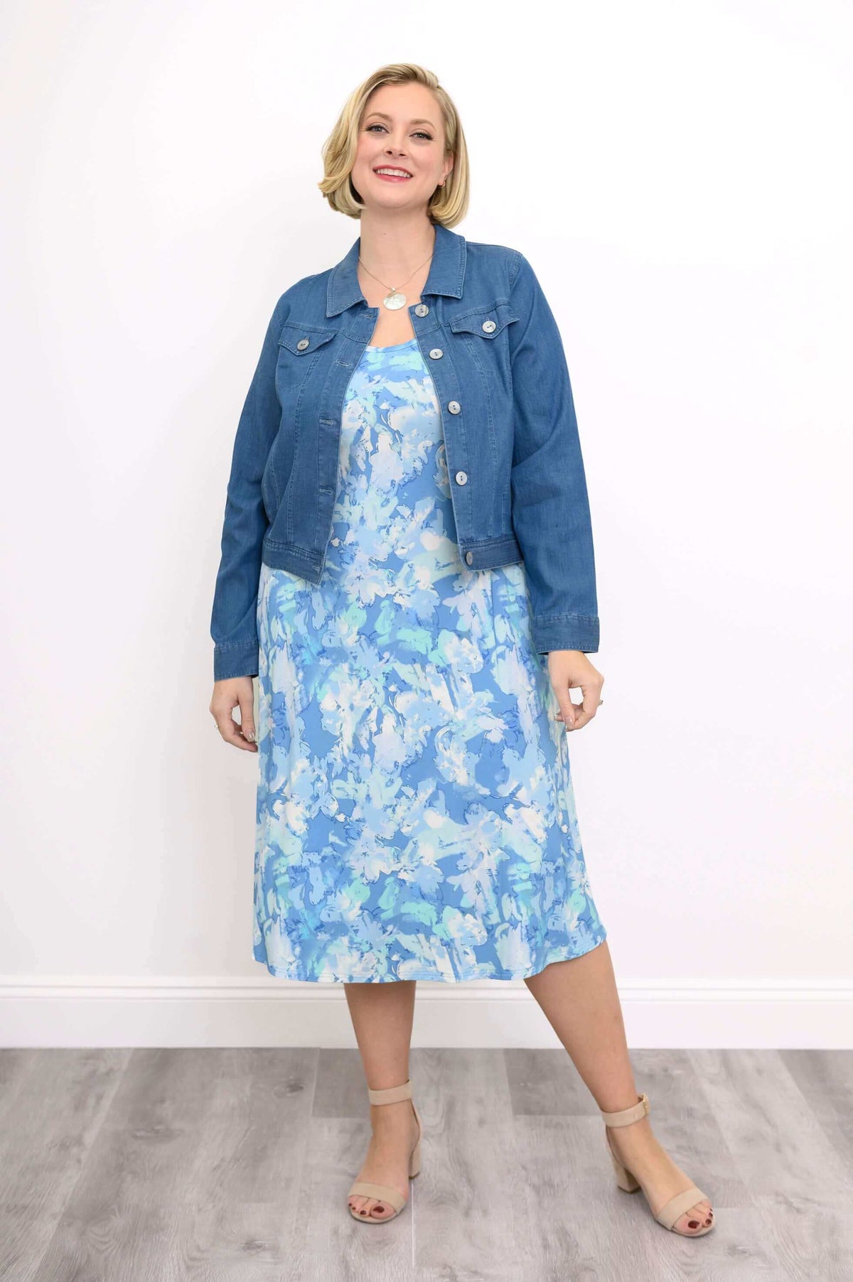 Woman styled in a blue denim jacket over a blue and white floral dress