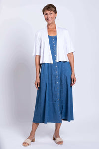 Woman standing in a blue denim maxi dress with a white cardigan, smiling