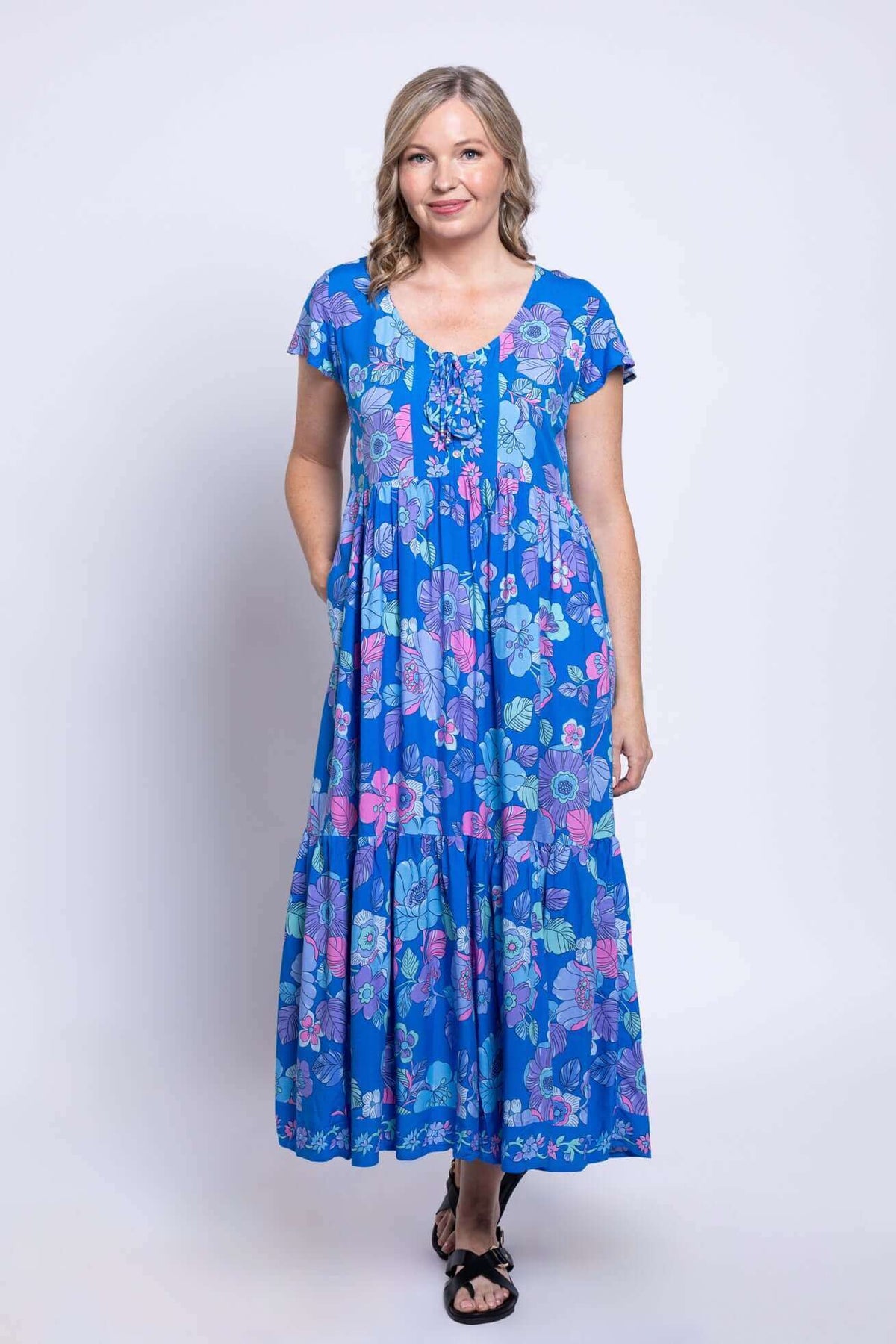 Front angled view of a woman in a blue floral Sharpie Dress with pockets and flutter sleeves