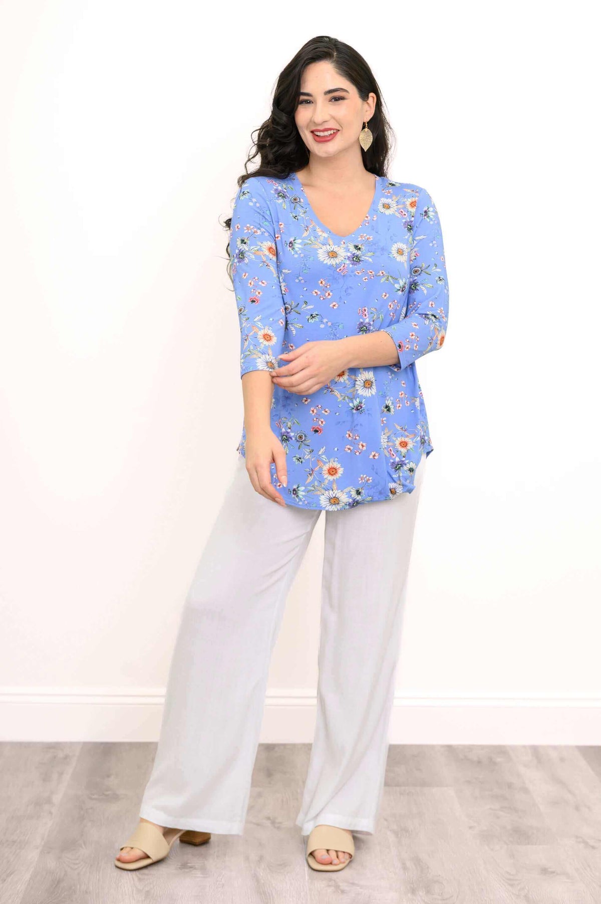 Woman modeling a blue floral V-neck top with white pants, arms crossed