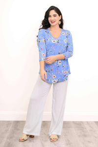 Woman modeling a blue floral V-neck top with white pants, arms crossed