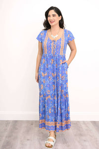 Woman posing in blue floral maxi dress with hands in pockets, side glance