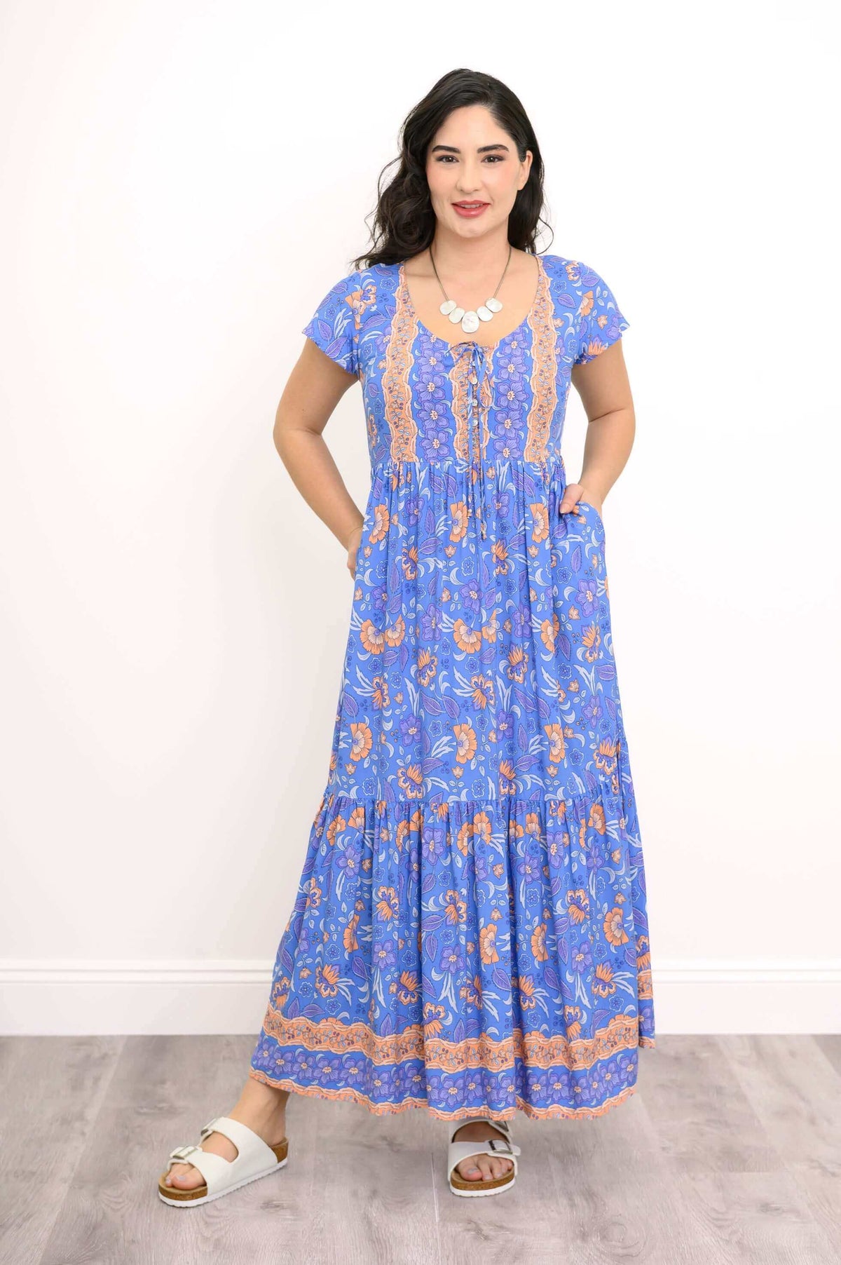 Blue floral maxi dress with peach accents, model with hands in pockets