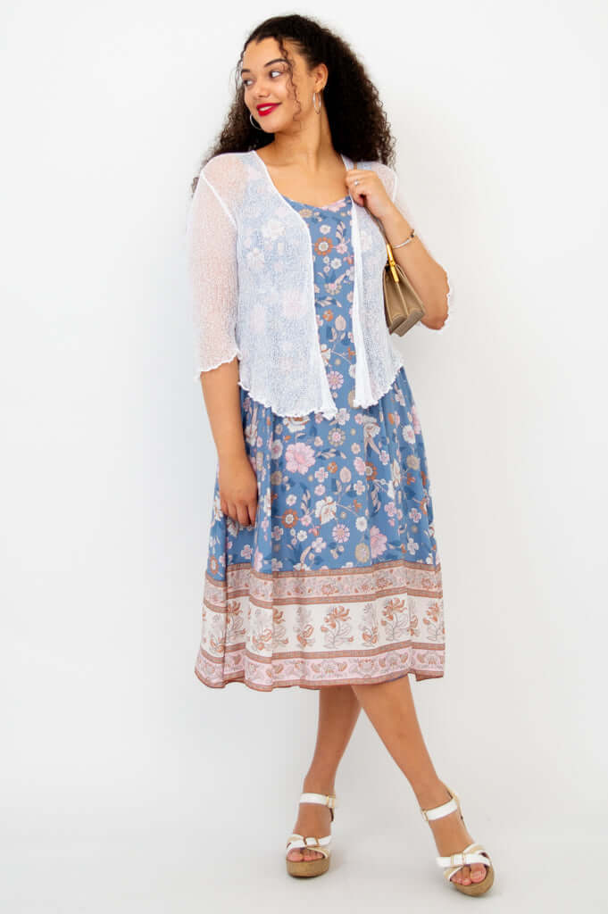 Woman in a blue floral dress paired with a short white shrug and tan bag
