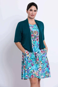 Woman in blue floral dress with teal cardigan, hands in pockets, close up