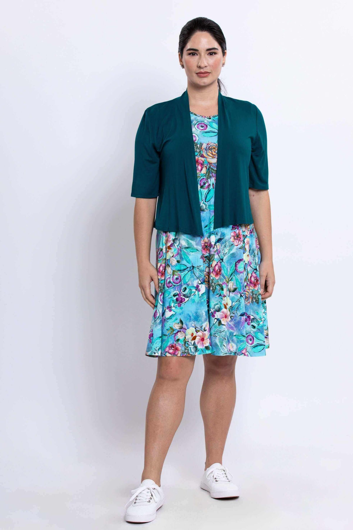 Woman in blue floral dress styled with a teal short-sleeve cardigan and white sneakers