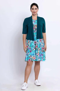 Woman in blue floral dress styled with a teal short-sleeve cardigan and white sneakers
