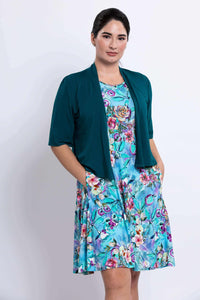 Woman in blue floral dress with teal jacket and hands in pockets