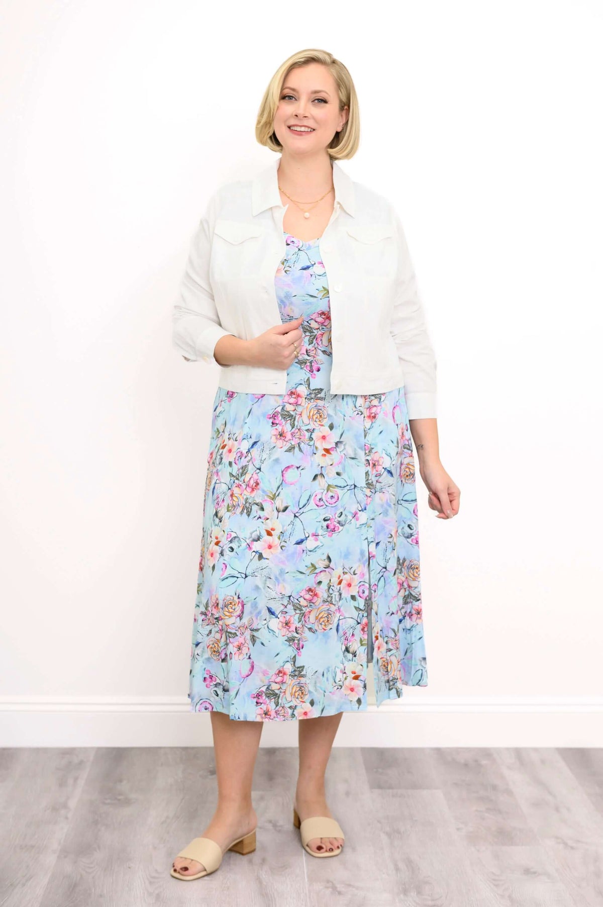 Woman wearing a blue floral dress with white cropped jacket, standing and smiling