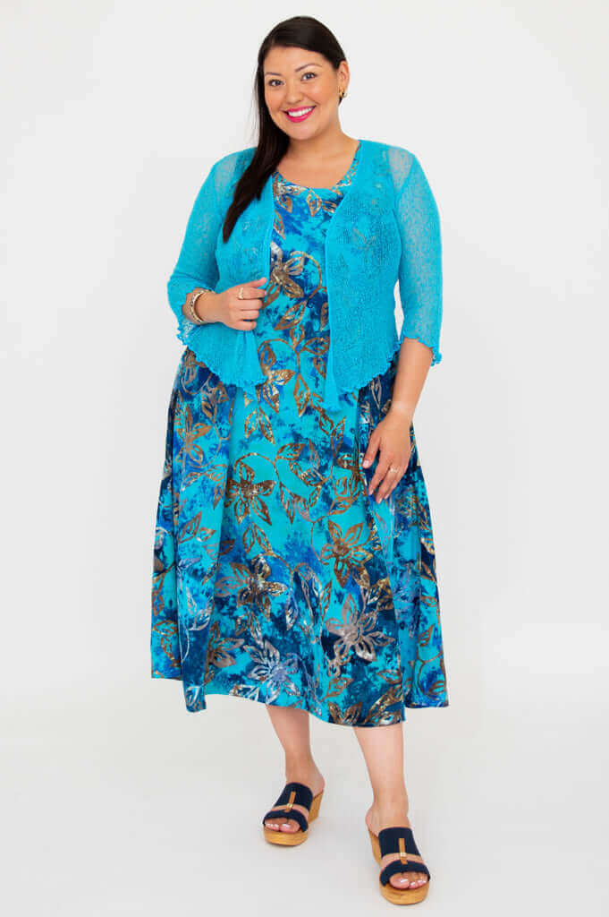 Woman wearing a blue floral midi dress with a textured blue cardigan, standing against a white background