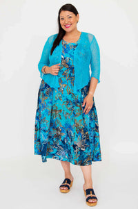 Woman wearing a blue floral midi dress with a textured blue cardigan, standing against a white background