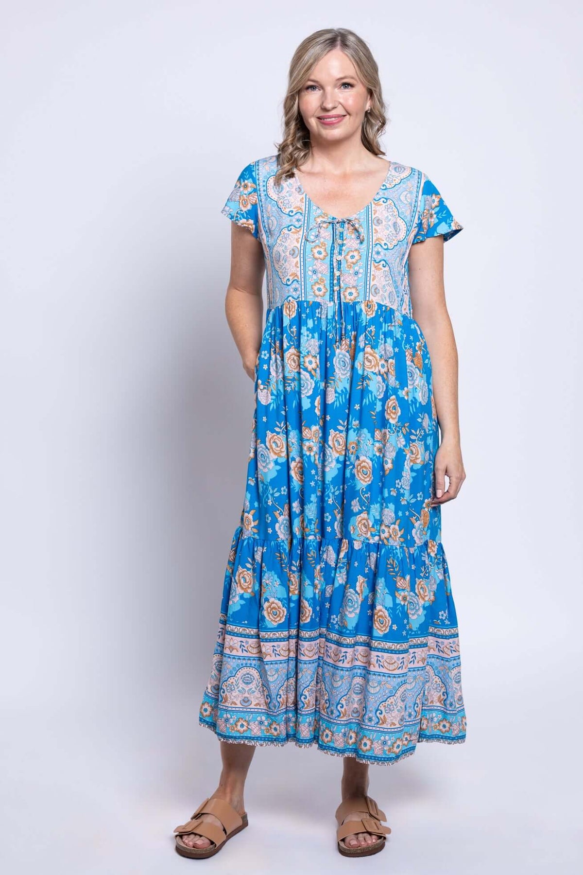Woman wearing a blue floral midi dress with flutter sleeves and tiered skirt, front view