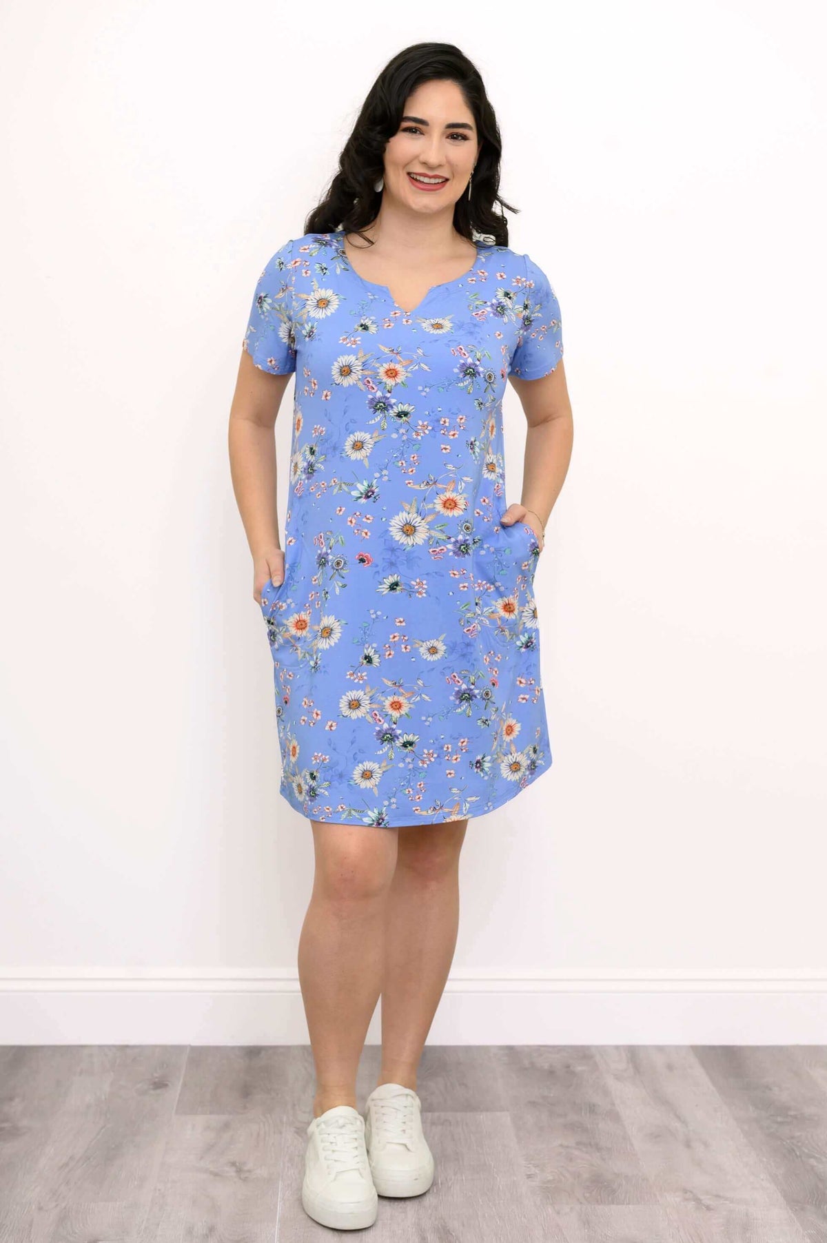 Model in blue floral shift dress with hands in pockets and white sneakers