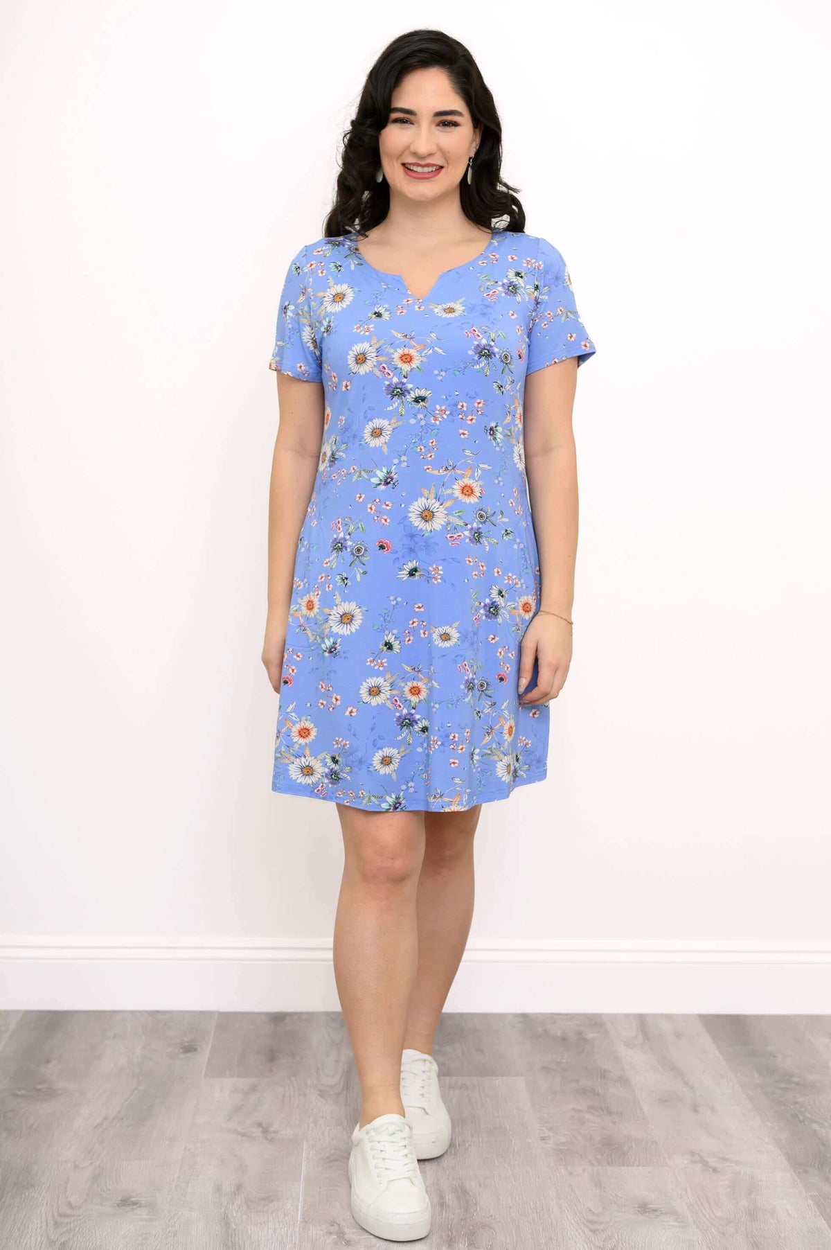 Model wearing a blue floral print shift dress with short sleeves and white sneakers