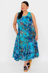 Woman posing in a blue floral sleeveless midi dress with one foot forward, against a white background