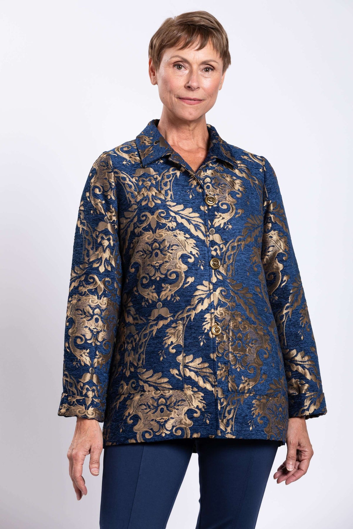 Woman wearing a blue jacquard coat with gold ornate pattern and brass buttons