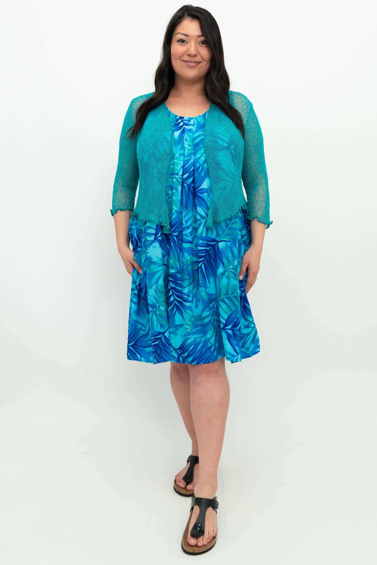 Front view of woman wearing the blue leaf pleated dress and teal cardigan